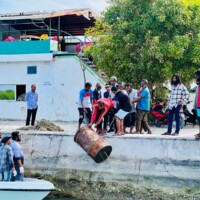 people pulling an oil barrel out of a lagoon