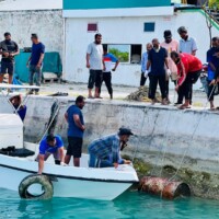 group of men pulling an oil barrel from the lagoon of Thimarafushi
