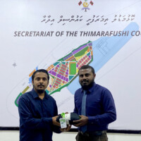 man in ocean blue shirt with a large mustache holding a uniform and a staff card