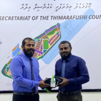 man in blue shirt smiling and holding a piece of uniform