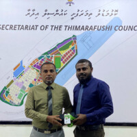 man giving staff card and a folded uniform to an angry man in an olive green shirt