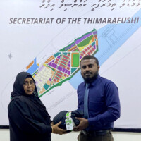 Thimarafushi council secretary general giving a folded uniform to an employee