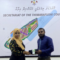 man handing a folded uniform to a woman in yellow burka