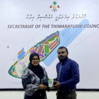 woman with glasses smiling at camera while holding a uniform